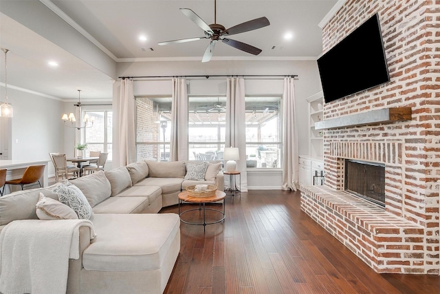 living room with crown molding, dark hardwood / wood-style floors, ceiling fan with notable chandelier, and a brick fireplace