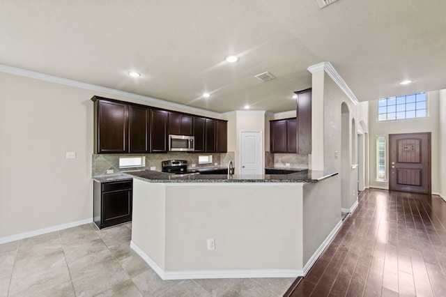 kitchen featuring crown molding, appliances with stainless steel finishes, kitchen peninsula, and dark stone counters