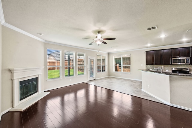 unfurnished living room with sink, crown molding, light hardwood / wood-style flooring, a textured ceiling, and ceiling fan