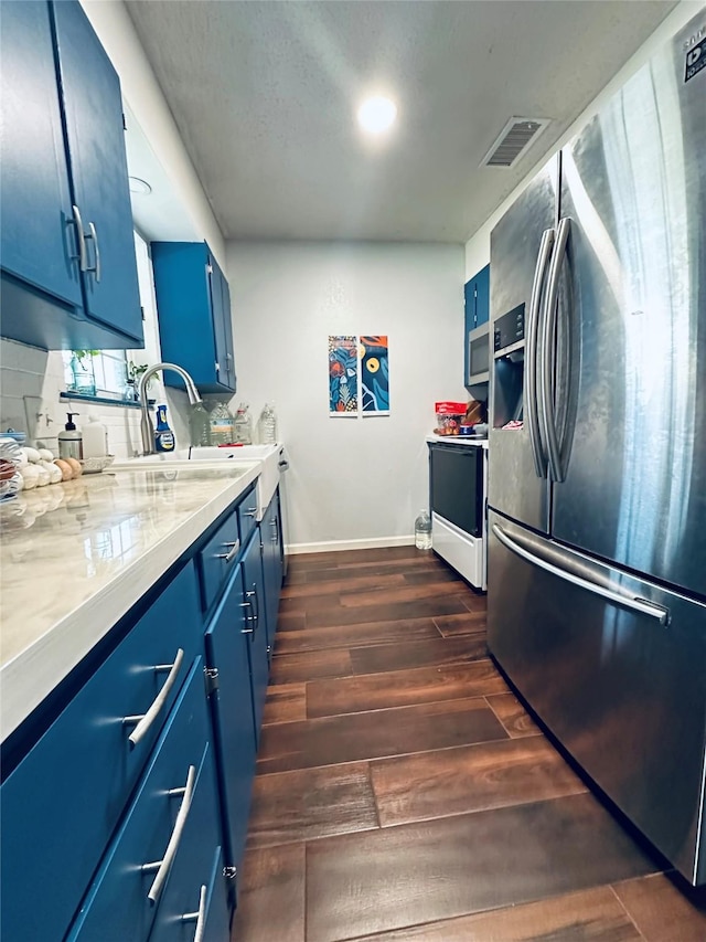 kitchen with blue cabinetry, sink, light stone counters, appliances with stainless steel finishes, and dark hardwood / wood-style floors