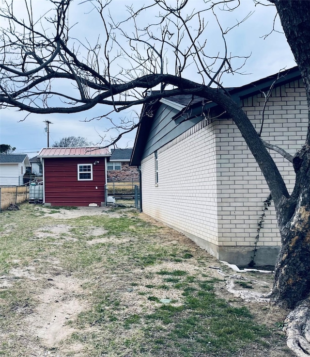 view of side of property featuring an outbuilding, a storage shed, brick siding, and fence