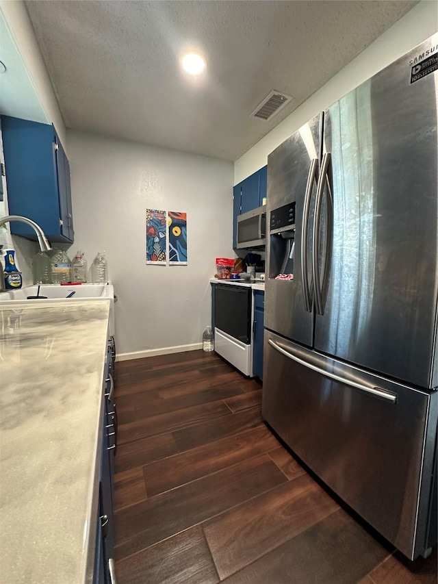 kitchen featuring sink, blue cabinetry, appliances with stainless steel finishes, a textured ceiling, and dark hardwood / wood-style flooring