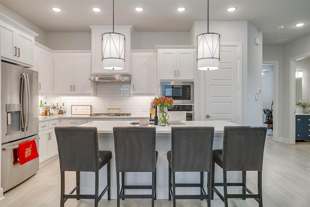 kitchen featuring stainless steel appliances, white cabinetry, a kitchen island with sink, and decorative light fixtures