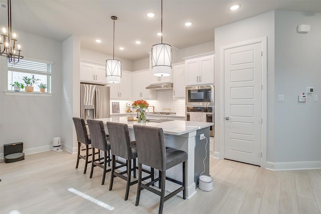 kitchen featuring pendant lighting, stainless steel appliances, an island with sink, and white cabinets