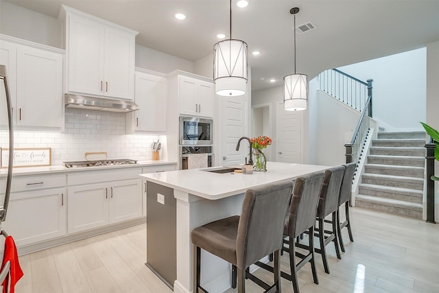 kitchen with stainless steel gas stovetop, white cabinetry, tasteful backsplash, hanging light fixtures, and a center island with sink