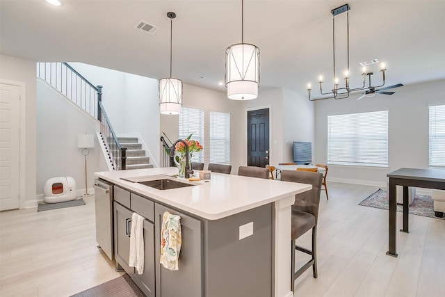 kitchen featuring a kitchen bar, sink, hanging light fixtures, light hardwood / wood-style flooring, and a kitchen island with sink