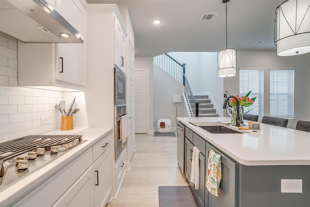 kitchen with an island with sink, sink, wall chimney range hood, and white cabinets