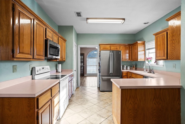 kitchen featuring light tile patterned flooring, stainless steel appliances, kitchen peninsula, and sink