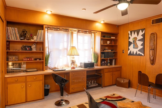 carpeted home office featuring built in desk, ornamental molding, wooden walls, and ceiling fan