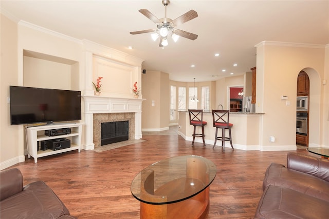 living room with ornamental molding, arched walkways, baseboards, and wood finished floors