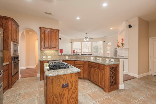 kitchen featuring arched walkways, stainless steel appliances, a sink, ceiling fan, and a kitchen island