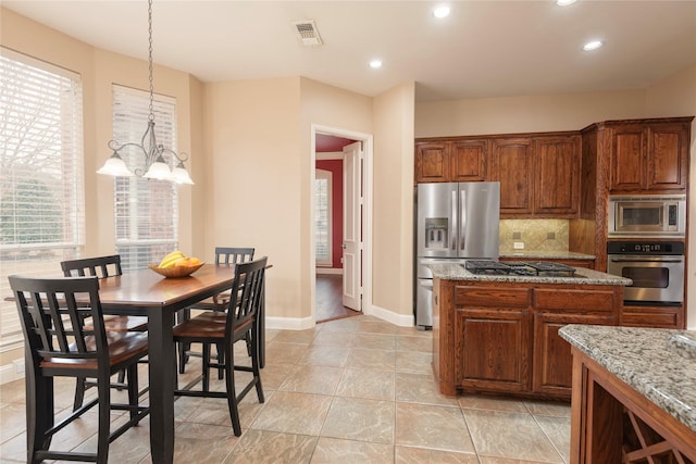 kitchen with light stone countertops, visible vents, appliances with stainless steel finishes, backsplash, and brown cabinets