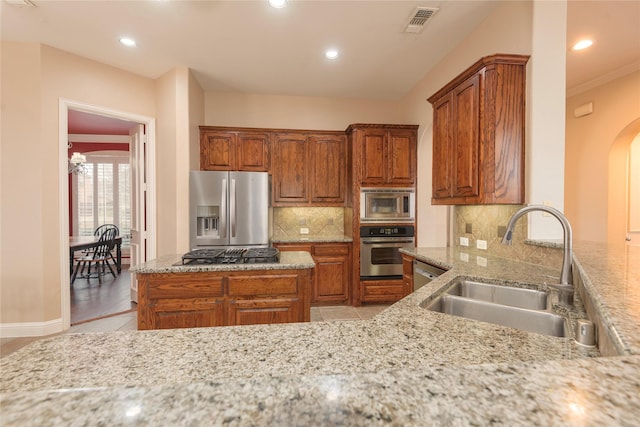 kitchen featuring stainless steel appliances, a sink, arched walkways, brown cabinetry, and decorative backsplash