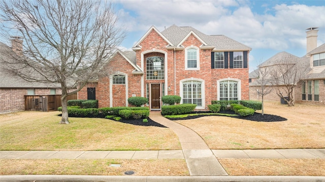 view of front of house with roof with shingles, brick siding, and a front lawn