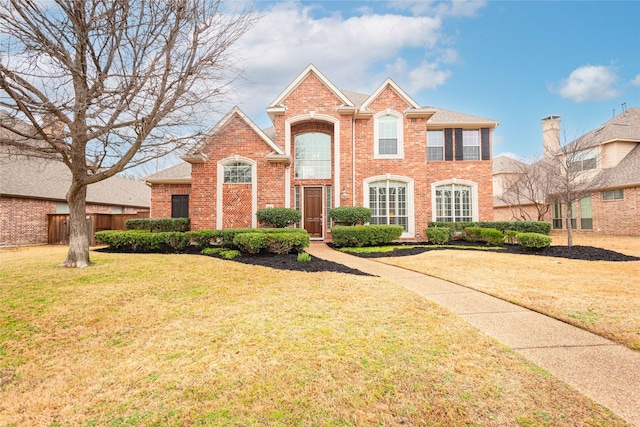 view of front of house featuring a shingled roof, a front yard, brick siding, and fence