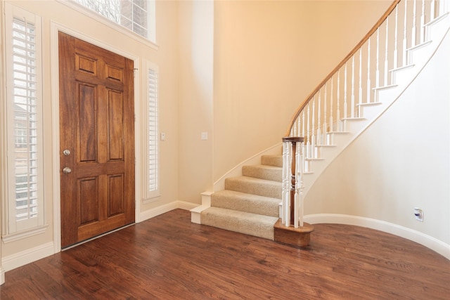 foyer entrance featuring wood finished floors, baseboards, stairs, and a high ceiling
