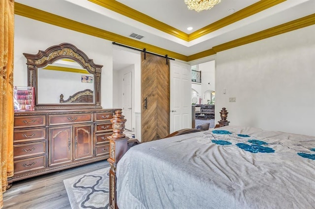 bedroom with a tray ceiling, light hardwood / wood-style flooring, ornamental molding, and a barn door