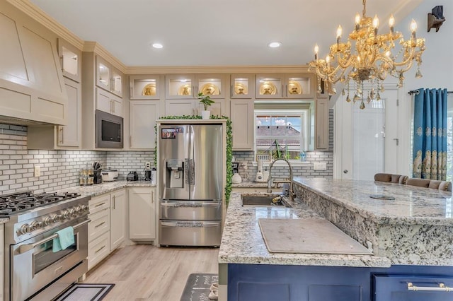 kitchen with sink, light stone counters, decorative light fixtures, custom range hood, and stainless steel appliances