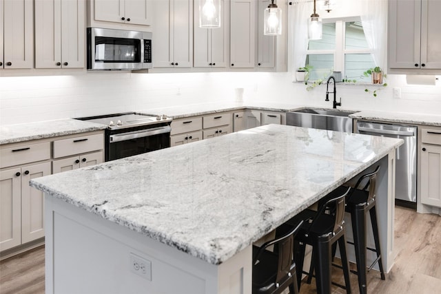 kitchen with sink, light stone counters, decorative light fixtures, a kitchen island, and stainless steel appliances