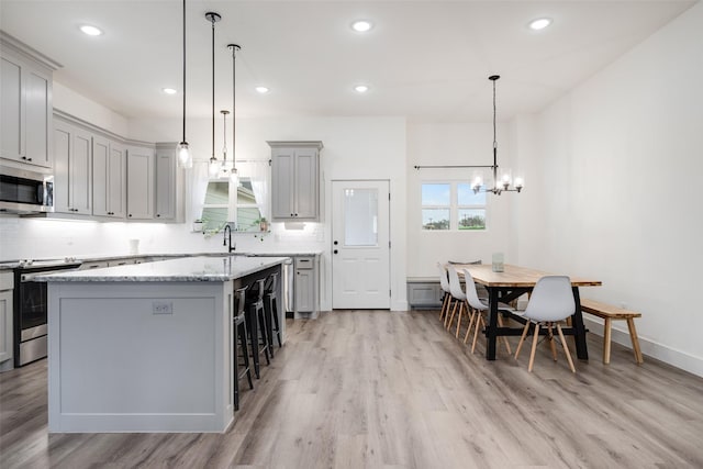 kitchen featuring gray cabinets, a kitchen island, appliances with stainless steel finishes, a breakfast bar, and pendant lighting