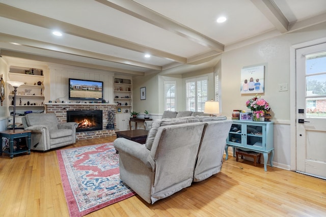 living room with beamed ceiling, a fireplace, built in shelves, and light hardwood / wood-style floors