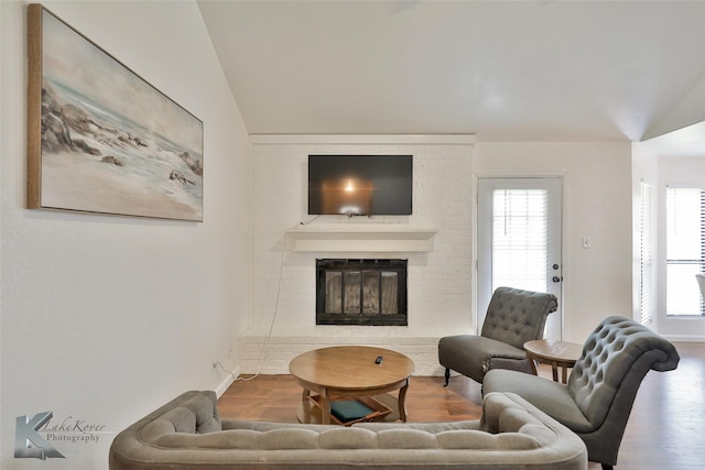 living room with hardwood / wood-style flooring, vaulted ceiling, a brick fireplace, and a wealth of natural light