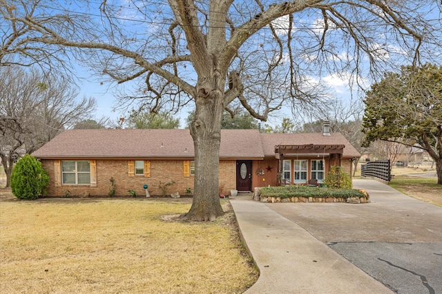 ranch-style house featuring brick siding, a shingled roof, driveway, a chimney, and a front yard