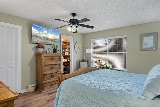 bedroom with a ceiling fan, a textured ceiling, baseboards, and wood finished floors