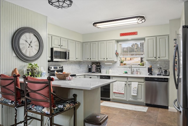 kitchen with a breakfast bar, light countertops, decorative backsplash, appliances with stainless steel finishes, and a sink