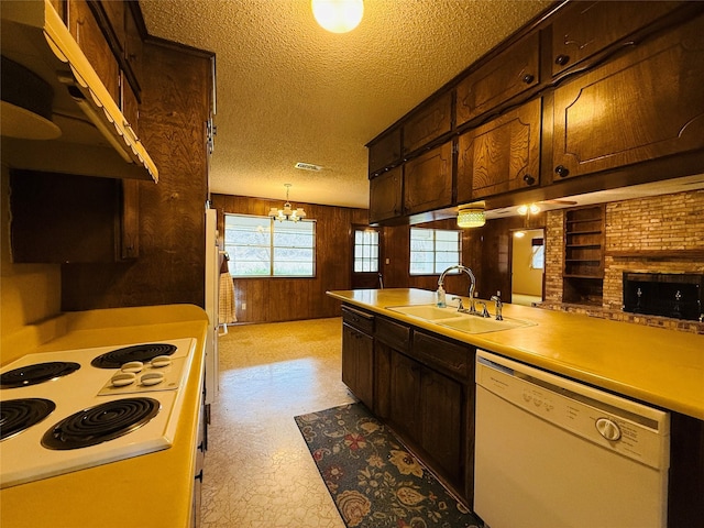 kitchen featuring white appliances, hanging light fixtures, light countertops, wood walls, and a sink