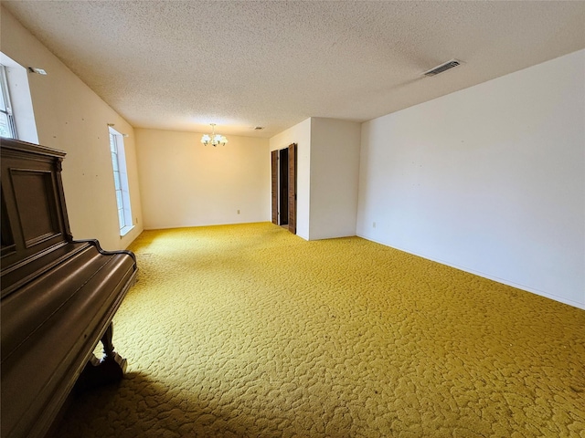 carpeted empty room with a textured ceiling, visible vents, and a notable chandelier