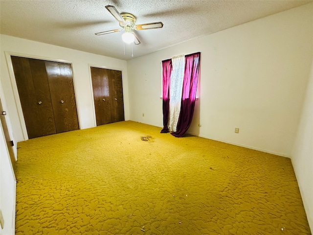 unfurnished bedroom featuring multiple closets, carpet floors, ceiling fan, and a textured ceiling