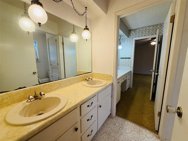 bathroom with double vanity, a sink, toilet, and wallpapered walls