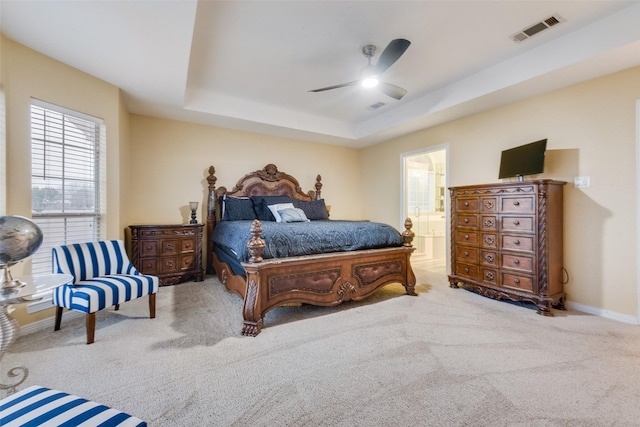 bedroom featuring ensuite bath, light colored carpet, ceiling fan, and a tray ceiling