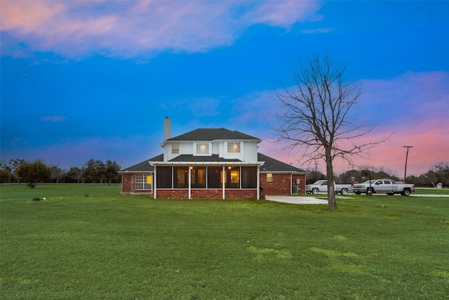 back house at dusk featuring a sunroom and a lawn