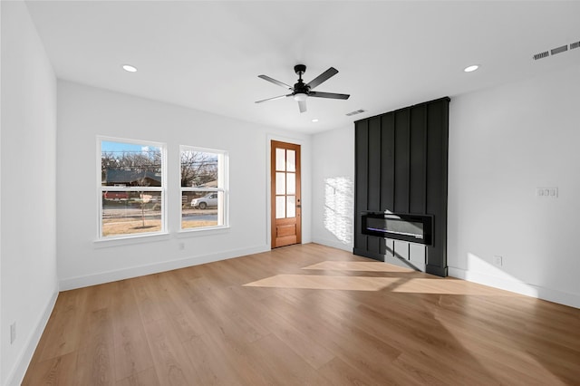 unfurnished living room with ceiling fan, a large fireplace, and light wood-type flooring