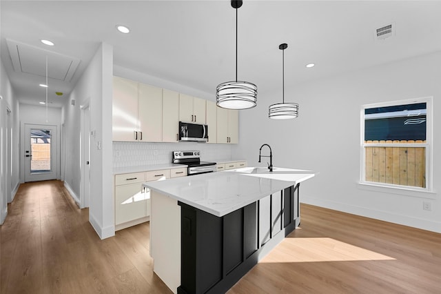 kitchen featuring an island with sink, decorative backsplash, hanging light fixtures, stainless steel appliances, and light hardwood / wood-style flooring