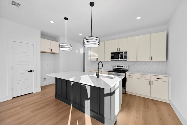 kitchen with pendant lighting, sink, stainless steel appliances, light hardwood / wood-style floors, and cream cabinetry