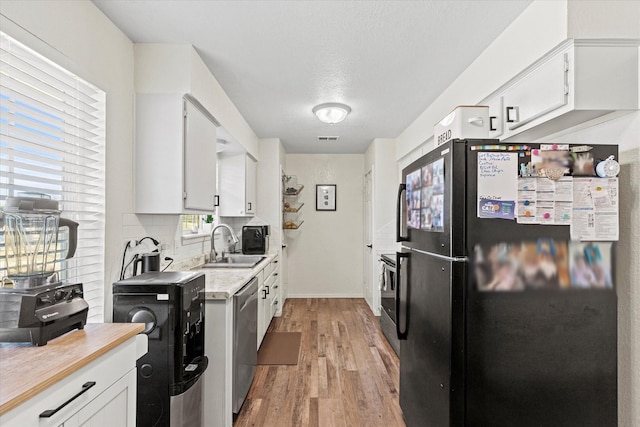 kitchen with stainless steel appliances, white cabinetry, sink, and light wood-type flooring