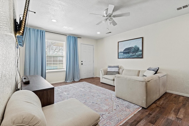 living room featuring ceiling fan, dark wood-type flooring, and a textured ceiling