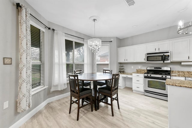 kitchen featuring appliances with stainless steel finishes, a notable chandelier, white cabinets, decorative light fixtures, and light wood-type flooring