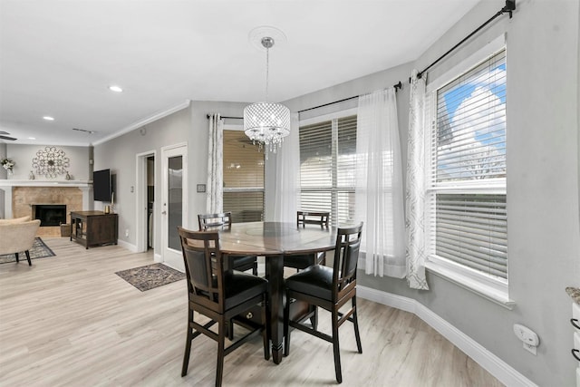 dining space with crown molding, a tiled fireplace, light hardwood / wood-style floors, and a notable chandelier