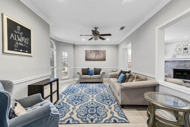 living room featuring light hardwood / wood-style flooring, crown molding, a stone fireplace, and ceiling fan