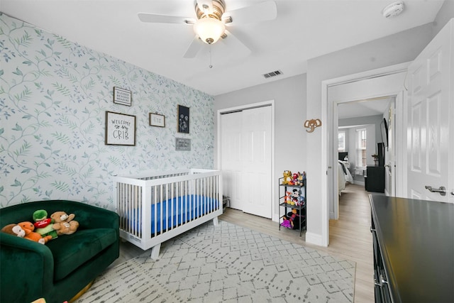 bedroom featuring ceiling fan, light hardwood / wood-style floors, a closet, and a crib