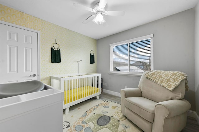 bedroom with a nursery area, ceiling fan, and hardwood / wood-style floors