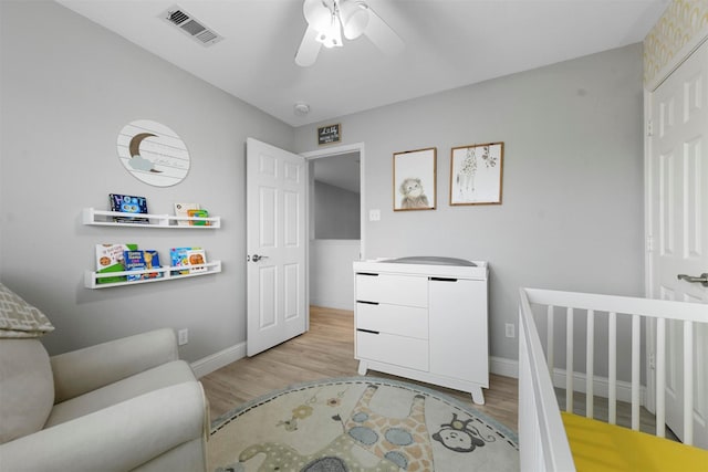 bedroom featuring a nursery area, ceiling fan, and light wood-type flooring