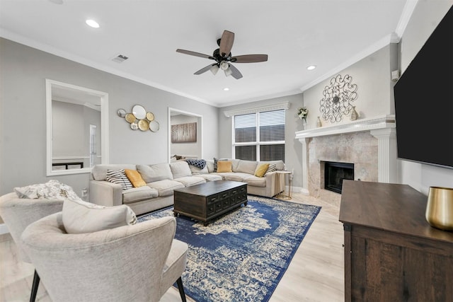 living room with a premium fireplace, crown molding, light wood-type flooring, and ceiling fan