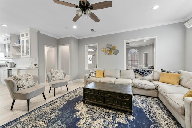 living room with crown molding, light hardwood / wood-style floors, ceiling fan, and bar area