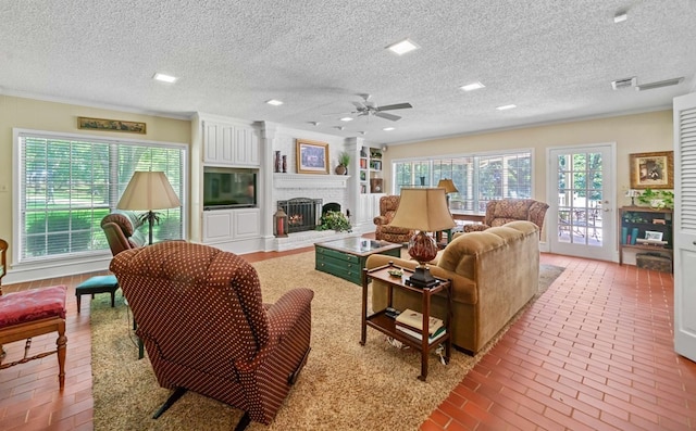 living room featuring ceiling fan, ornamental molding, a brick fireplace, and a textured ceiling