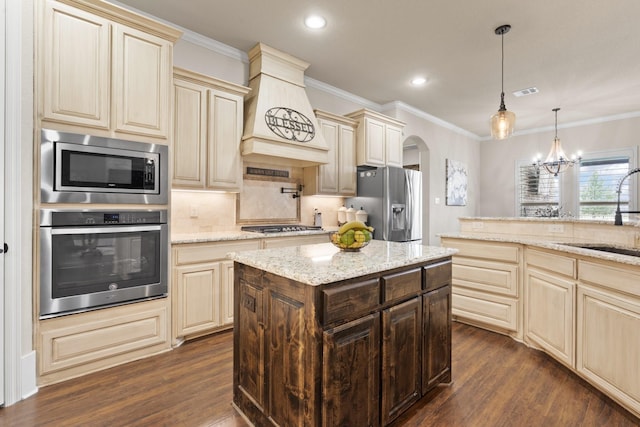 kitchen with arched walkways, cream cabinets, stainless steel appliances, a sink, and tasteful backsplash